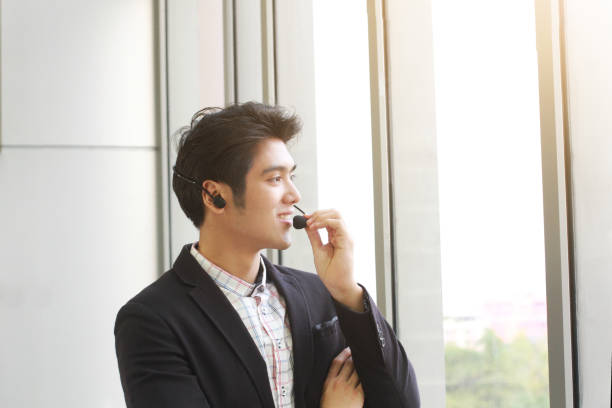 istock Smiling handsome Businessman Call Center standing near glass wall. Technical Support staff. Asian customer support team. 1263137617
