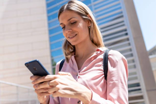 istock Smiling young woman using her mobile phone while standing in the street. 1263143883