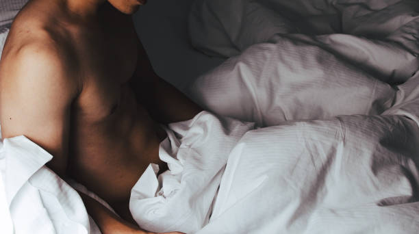 白いシーツで覆われたベッドに横たわっている裸の無駄のない筋肉の男 - 2113 ストックフォトと画像