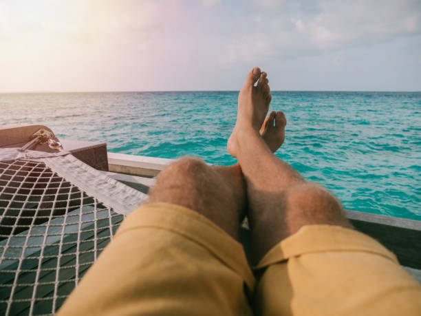 Pov of man relaxing on sea hammock View of man's feet hanging on hammock over sea in the Maldives, people enjoying luxury vacations staycation hotel asian stock pictures, royalty-free photos & images