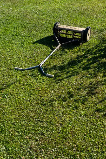 Photo of Retro mechanical lawn mower mows green grass on grass in bright evening sun