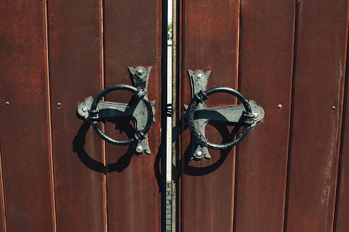 Old wooden gates with forged metallic vintage round handles closeup