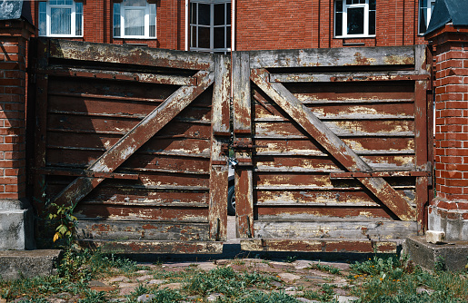 Shabby wooden gates with a lock near red brick country house