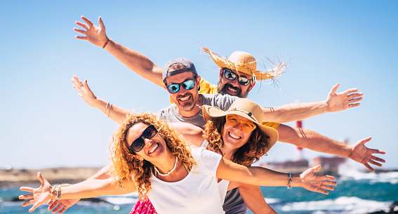 Group of happy people enjoy travel and summer holiday vacation together having fun under the sun - blue ocean water in background and sky - joyful adults smile with cheerful expressions