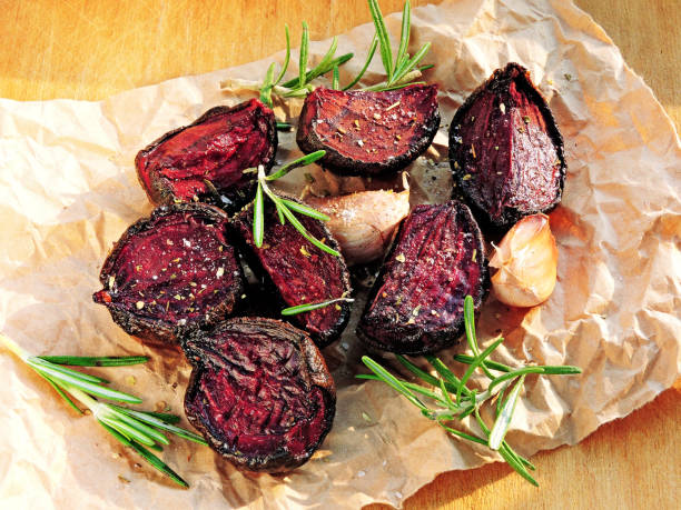 Baked beets on paper. Fresh rosemary. Pieces of baked beet. stock photo