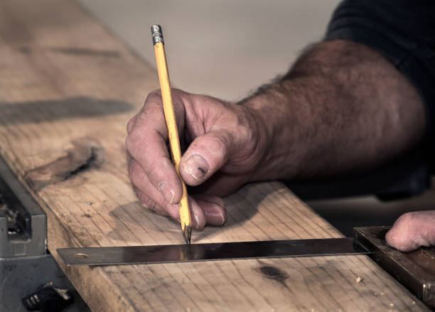 istock Male carpenter marks a line on a wooden board to cut while on construction job site 1263160017