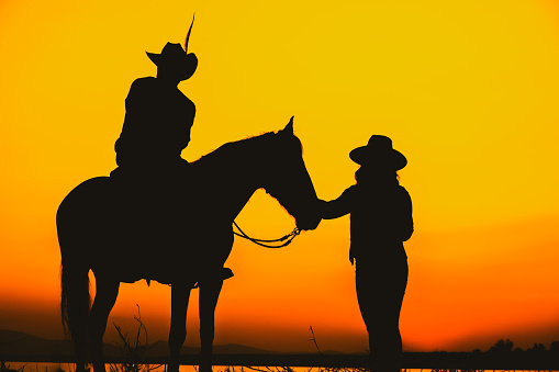 Silhouette Cowboy and  horse with sunset. A beautiful sunset silhouette of cowboys riding horseback with mountain range background during golden hours on the field.