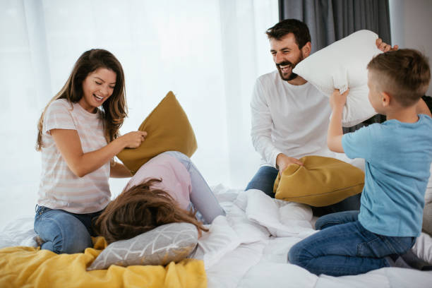 familia feliz tener una foto de acción de lucha de almohadas - bed couple pillow fight men fotografías e imágenes de stock