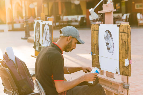 Egypt, Hurghada - painter artist at sunset street working with canvas at artworks portraits on background