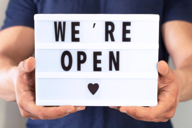 istock End of quarantine. Man holding lightbox with greeting text message We're open in his hands. Hotel, cafe, local shop, service owner welcoming guests after coronavirus outbreak and people shutdown. 1263166708