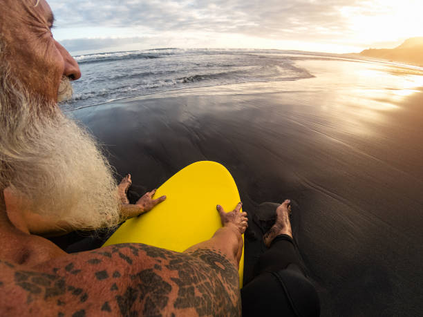 istock Happy fit senior man sitting on surfboard watching sunset time - Back view bearded surfer having fun on surfing day - Extreme sport and health people lifestyle concept 1263168931