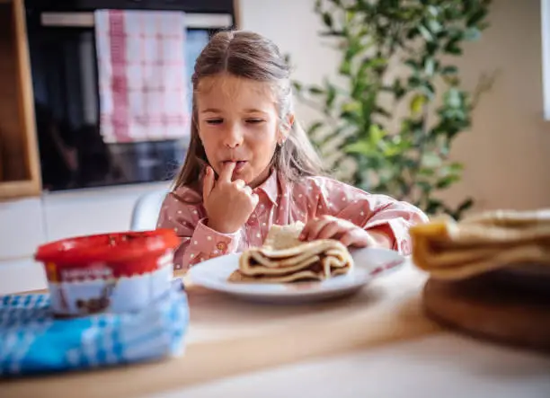 Cute little toddler girl eating homemade fresh crepes or pancakes with chocolate cream