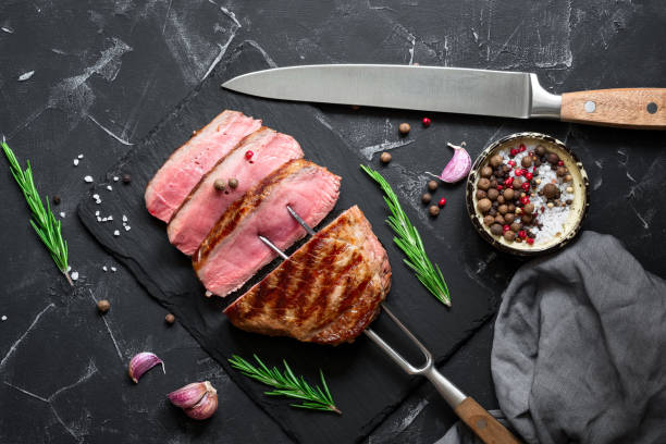 istock Grilled ribeye beef steak medium rare on the fork, black stone background. Top view, flat lay, copy space. 1263176879