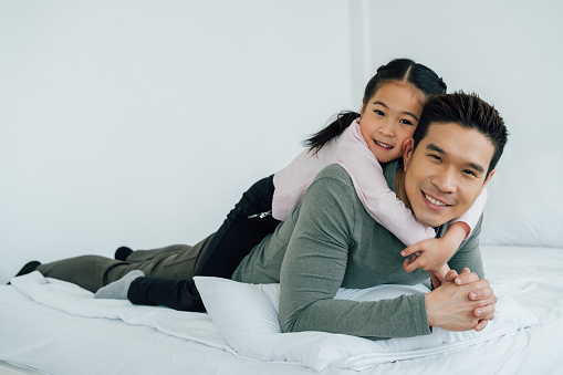 Cheerful Chinese girl lying on father's back looking at camera