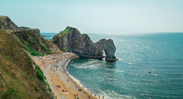 Durdle Door, Jurassic Coast near Lulworth in Dorset, England - a natural limestone arch. Durdle Door with people relaxing on the beach on a sunny day in August 2020. weymouth dorset stock pictures, royalty-free photos & images