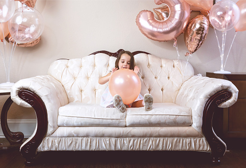 3-year-old birthday girl playing with her balloons on the couch