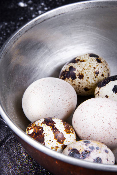 A few eggs next to a few quail eggs in a bowl or basket.