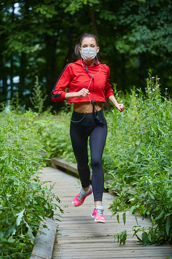 girl in a mask and sportswear jogging on a wooden path in a forest park.