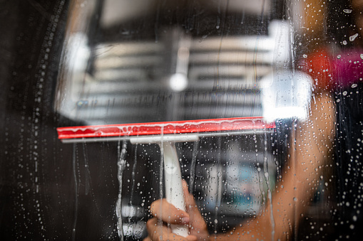 Male hand cleaning glass window pane in bathroom with shower squeegee