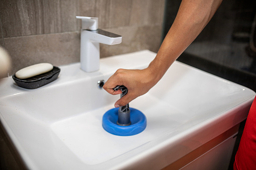 unblocking a clogged sink with a small blue plunger