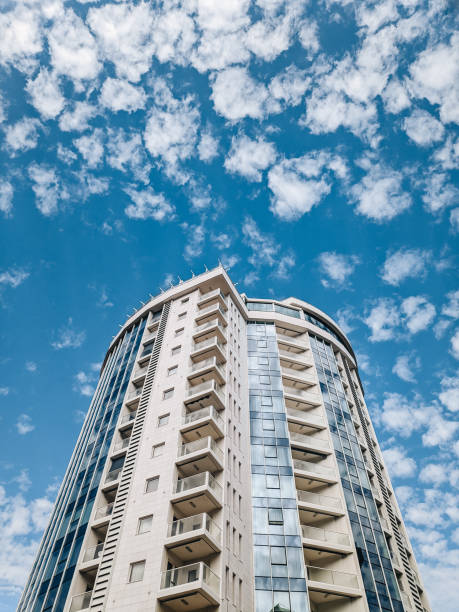 istock A multi-storey circular building with blue windows against a background of blue sky and white clouds. 1263227546
