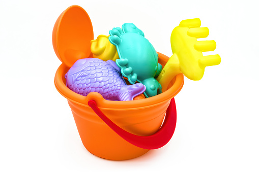 Beach toys: children's sea bucket with orange scoop, yellow rake, and various molds isolated on white background