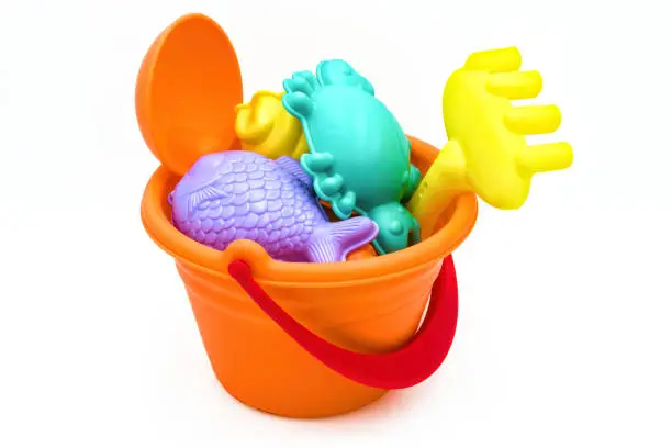 Photo of Beach toys: children's sea bucket with orange scoop, yellow rake, and various molds isolated on white background