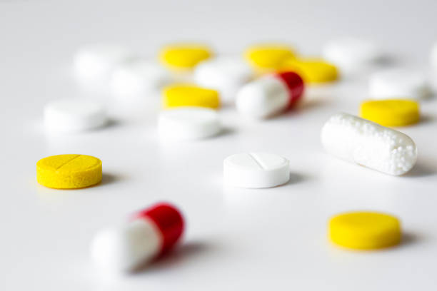 close up of yellow and red tablets and pills scattered on white table. - antibiotic red medicine healthcare and medicine imagens e fotografias de stock