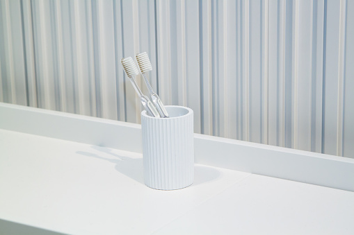 two toothbrushes in white white cup in bathroom on striped background