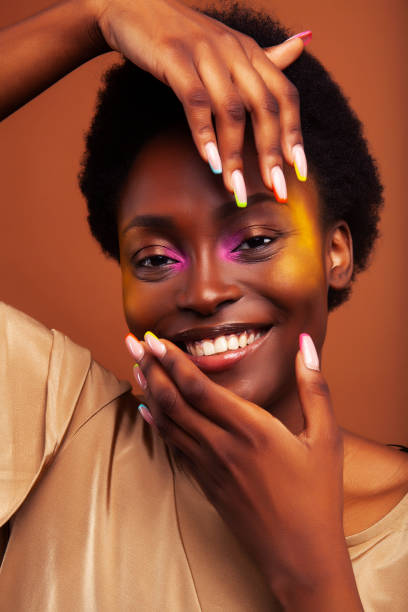 young pretty african girl with bright colorful makeup and manicure posing cheeful on brown background, lifestyle people concept stock photo
