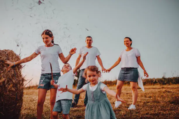 Photo of Family in shorts and T-shirts jump on haystacks