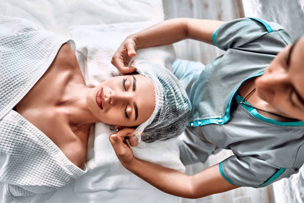 Young cute girl lying on a medical couch and getting ready putting on a hat. Young cute girl lying on a medical couch and getting ready putting on a hat. Beautician prepares the patient for a cosmetic procedure. Top view sports training clinic stock pictures, royalty-free photos & images