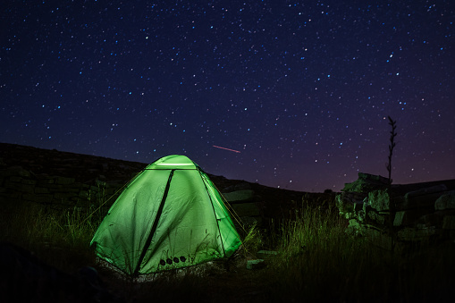 Camping tent near the Dinara mountain -highest point of Croatia in the Dinaric Alps with light inside is on the mountain valley under night starry sky. Trekking with backpacks night concept image.