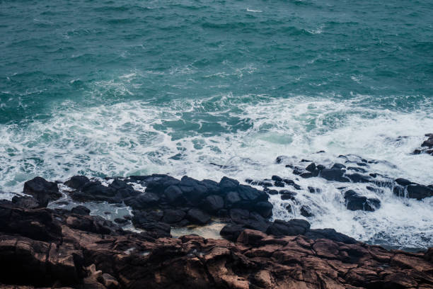 Aerial view of crashing waves on rocks. Background texture of a rocky shore and blue and turquoise sea