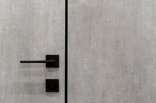 Close up of minimalist handle on closed grey door in house. Modern interior design with copy space wall