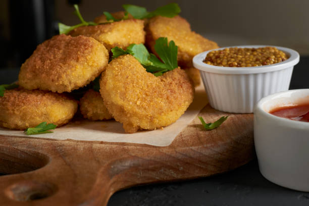 istock Appetizing chicken nuggets on a cutting board with parchment paper sprinkled with parsley leaves and tomato sauce and mustard seeds 1263294908