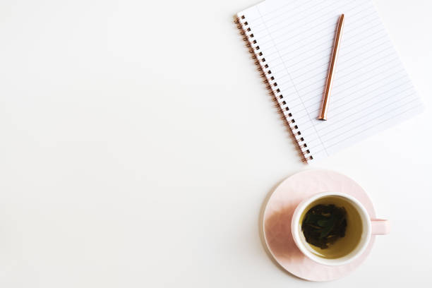istock Minimal flat lay with green tea in a pink cup, notepad with empty pages and metal pen on white table, space for text 1263303109