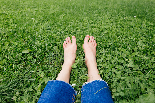 Legs woman relaxing on grass. Female feet on green grass background. Barefoot legs in the morning dew on the grass.