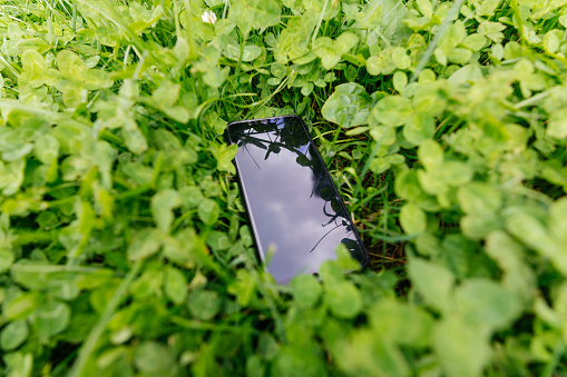 Blank screen mobile phone with copy space on a green grass background. Someone lost a phone in the park
