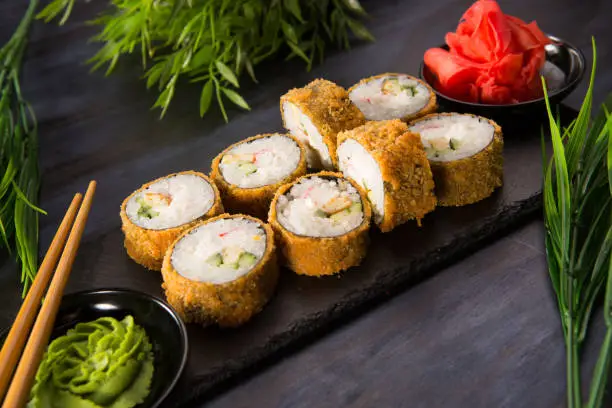 Set of fried sushi rolls with wasabi and ginger on a black background. Japanese oriental cuisine
