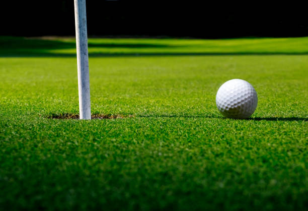 Golf field with a ball next to the hole and flag with long shadows on green grass. stock photo