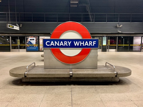 Canary Wharf underground.  Taken inside the station on the platform.  The Canary Wharf underground sign and bench on an empty platform.