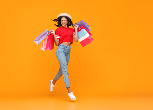 concept of shopping purchases and sales of happy young ethnic girl with packages jumping  on yellow background