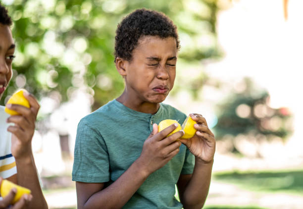 Two boys are playing with a lemon on a sunny day, one put a lemon in his eyes