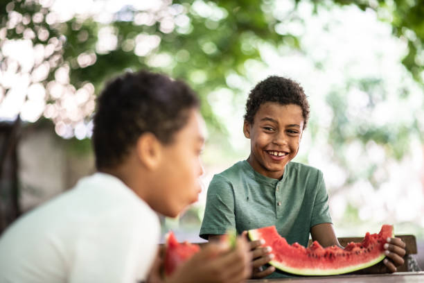 istock Two boys are sitting at a table eating a watermelon, talking and laughing 1263348173