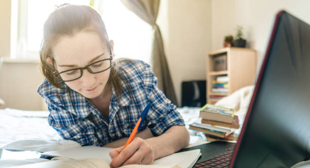 istock Student is passing online lesson on the Internet at home lying on a bed. Remote learning in schools and universities 1263353882