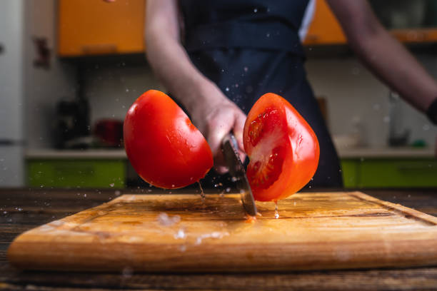 Chef cutting a red tomato in half with a knife. Splashes of juice fly in different directions and freeze in the air stock photo