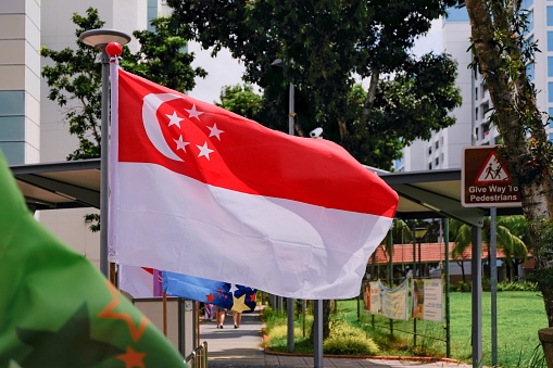 View of Singapore flag waving in the wind on bright sunny day in HDB neighbourhood. Selective focus