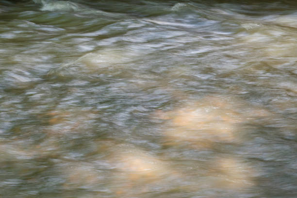 Blurred background with the surface of a fast flowing mountain river. A shallow clear mountain stream through which the stones at the bottom are visible.