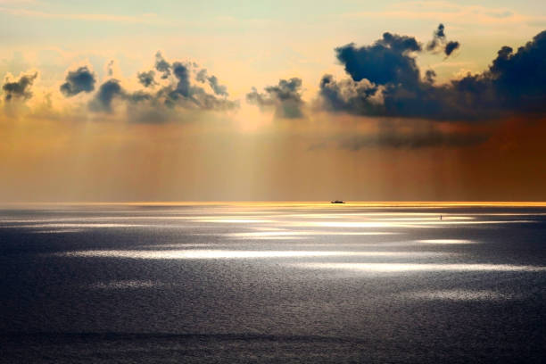 spots of light seeping into the sea at sunset with a ship on the golden horizon stock photo